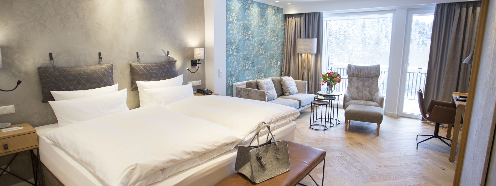 Room in blue/grey tones with double bed, couch and reading chair at Jagdhaus Wiese