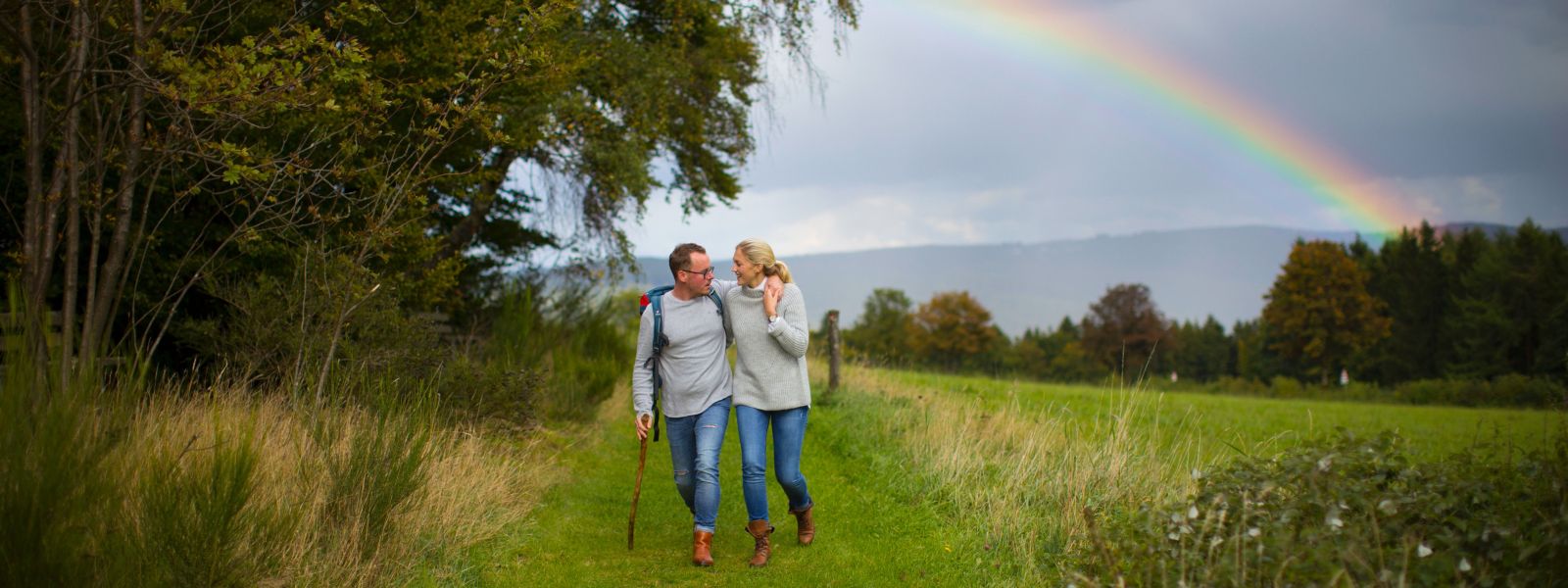 Wandelend paar op veldweg met regenboog op de achtergrond