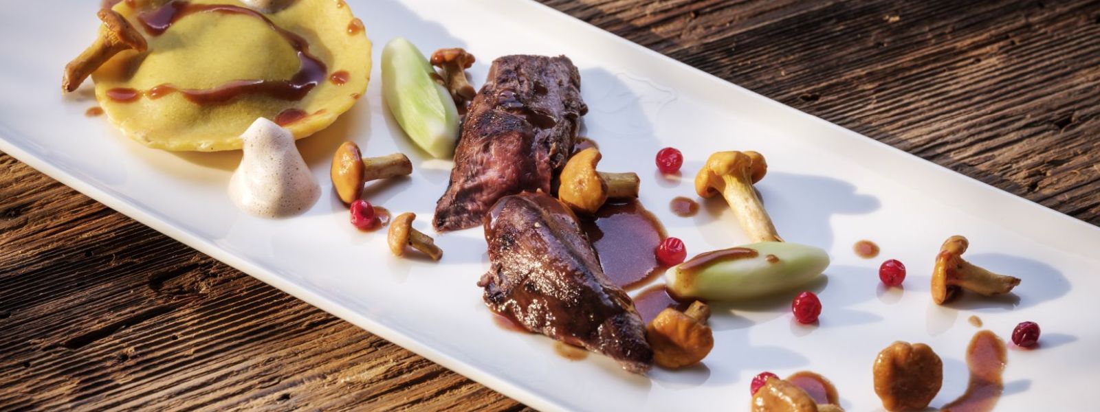 Vlees geserveerd in het midden van een langwerpig bord met cantharellen, tortellini en saus