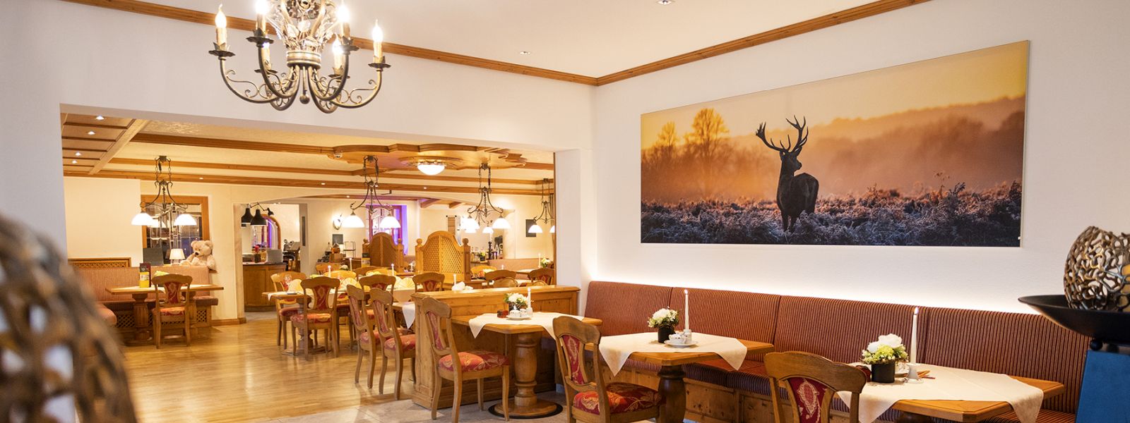 View into the restaurant of the Hotel Voss; many tables with white flowers; in the foreground a picture of a stag in the morning mood with fog and hoarfrost
