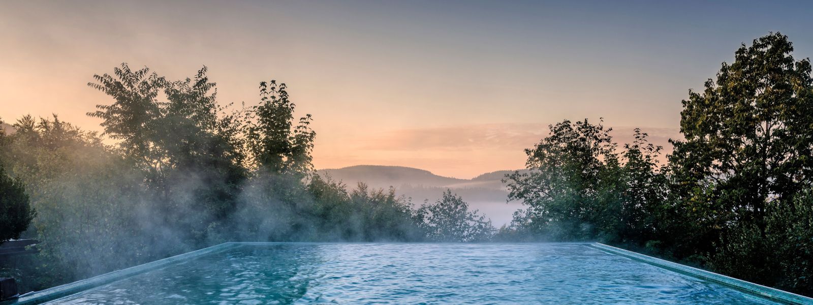 Infinity outdoor pool at sunrise, steam rises from the heated pool