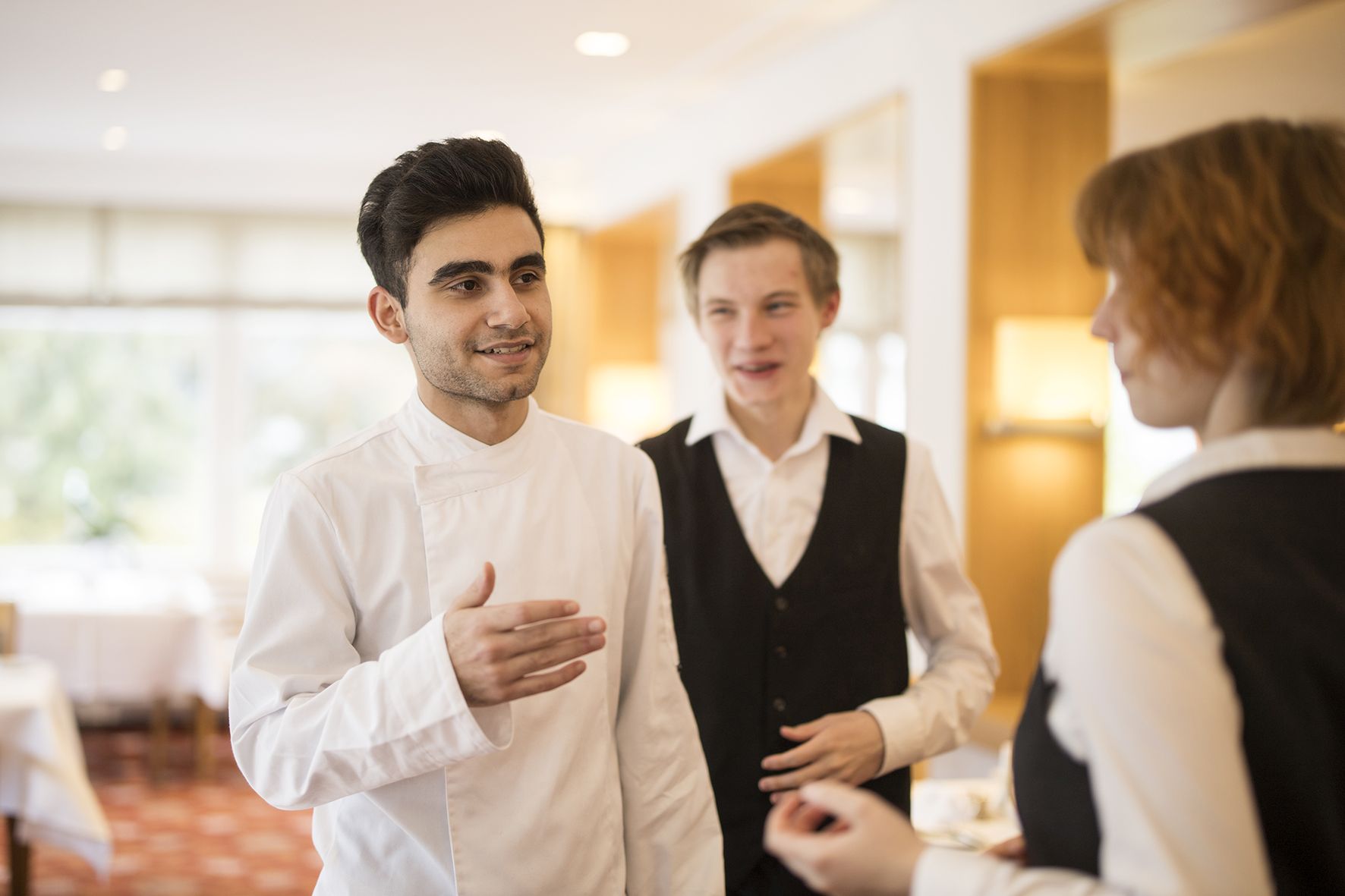 Apprentices from the kitchen and service are talking and standing in the restaurant.