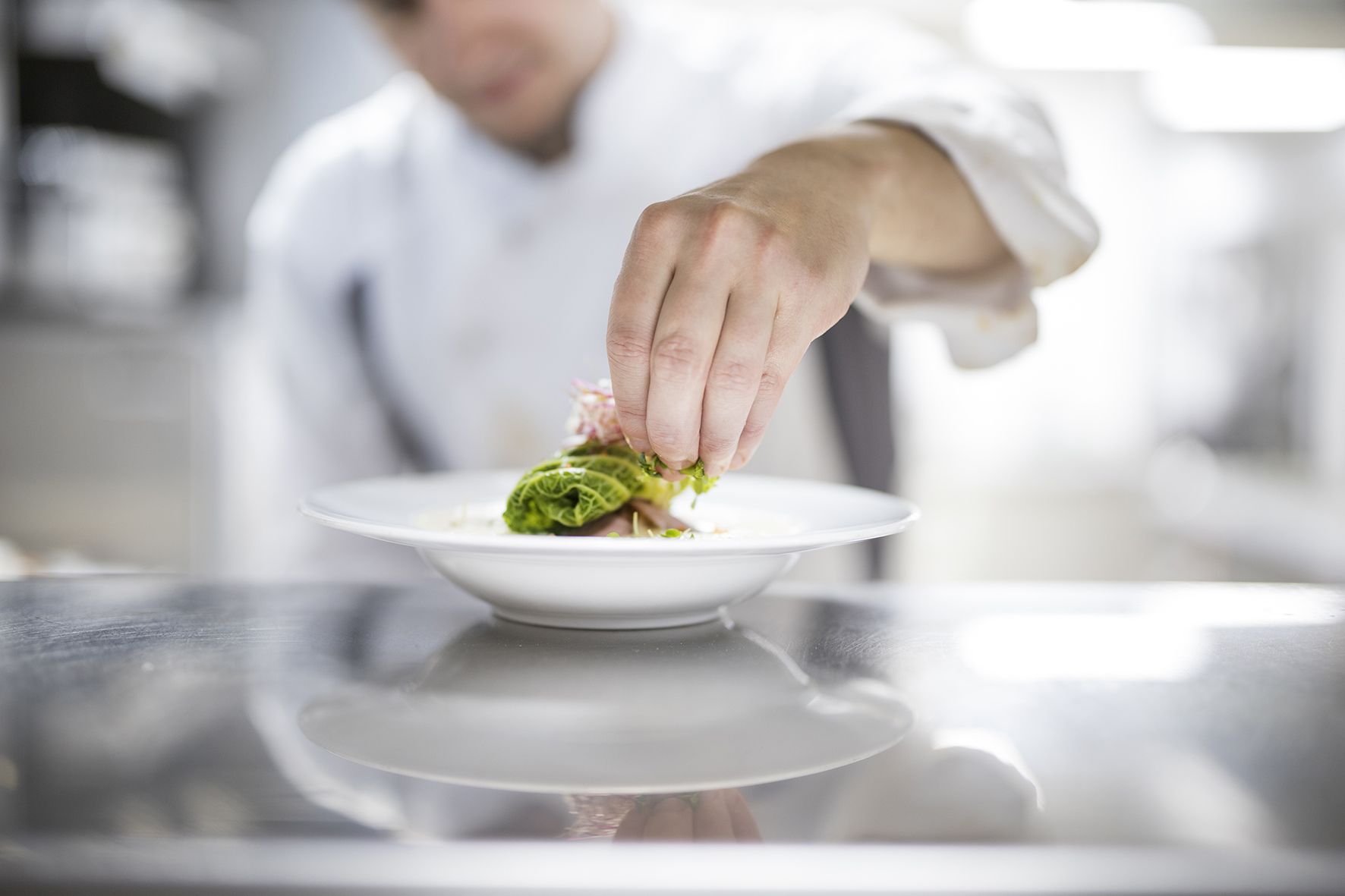 A chef sprinkles herbs over an arranged dish in a round plate.