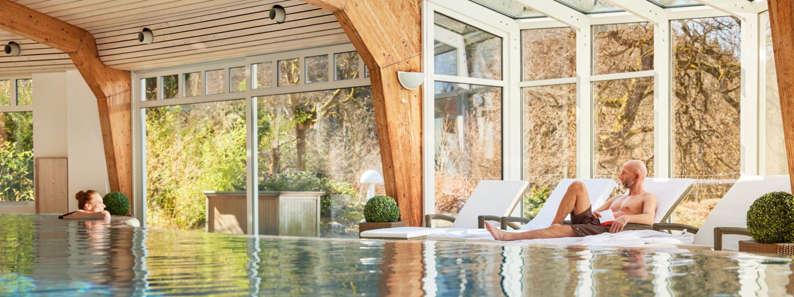 Swimming pool Jagdhaus Wiese- woman is in the pool at the edge of the pool and man is sitting on a deck chair, both are looking at each other
