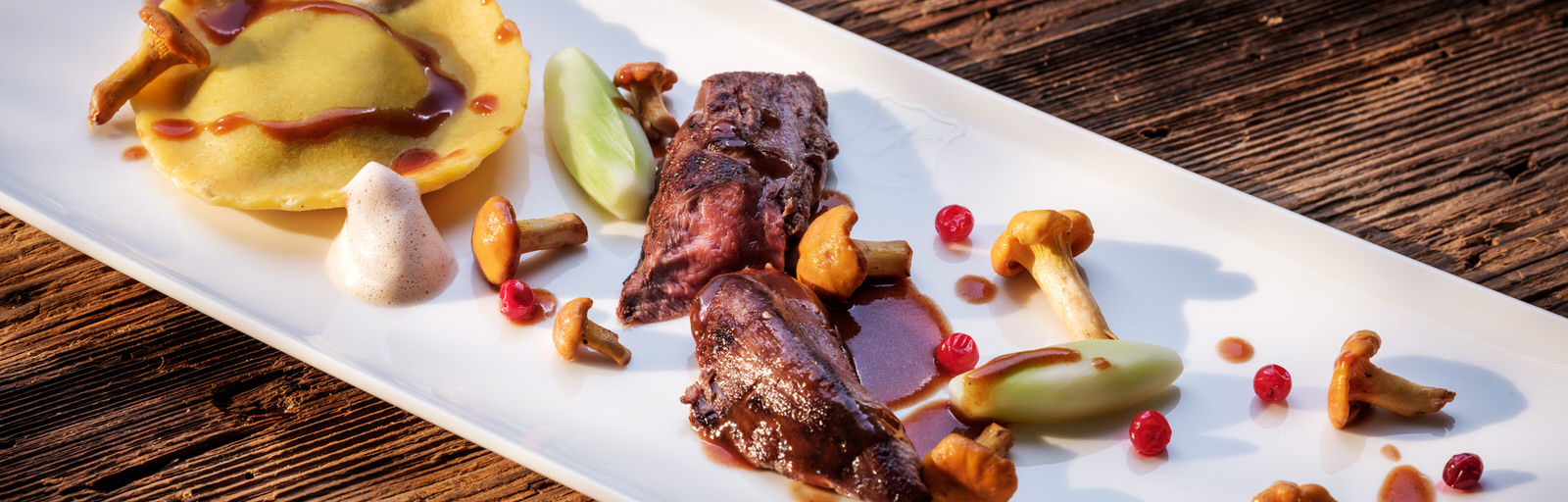 Meat arranged in the middle of an oblong plate with chanterelles, tortellini