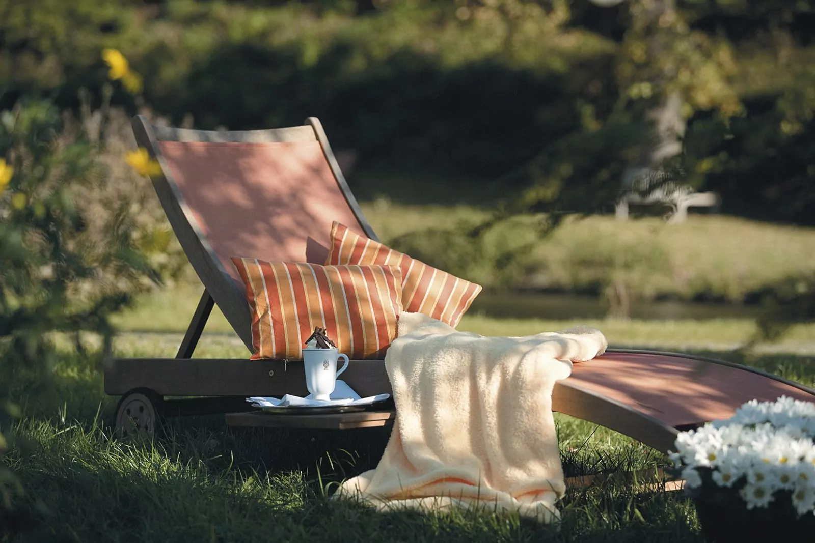 Liegestuhl im Hotelgarten mit bunten Kissen, Decke und Tasse Schokolade (Sommer)