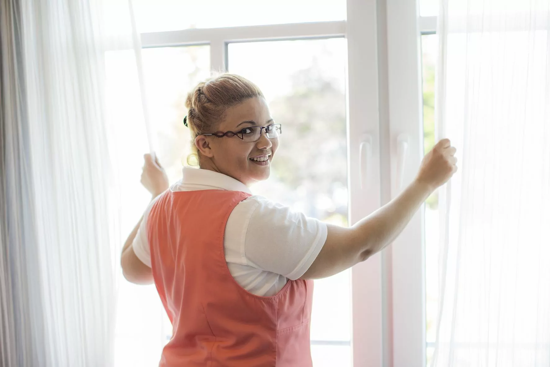 Die Hausdame schließt nach dem Lüften die Gardinen am Fenster eines Zimmers.