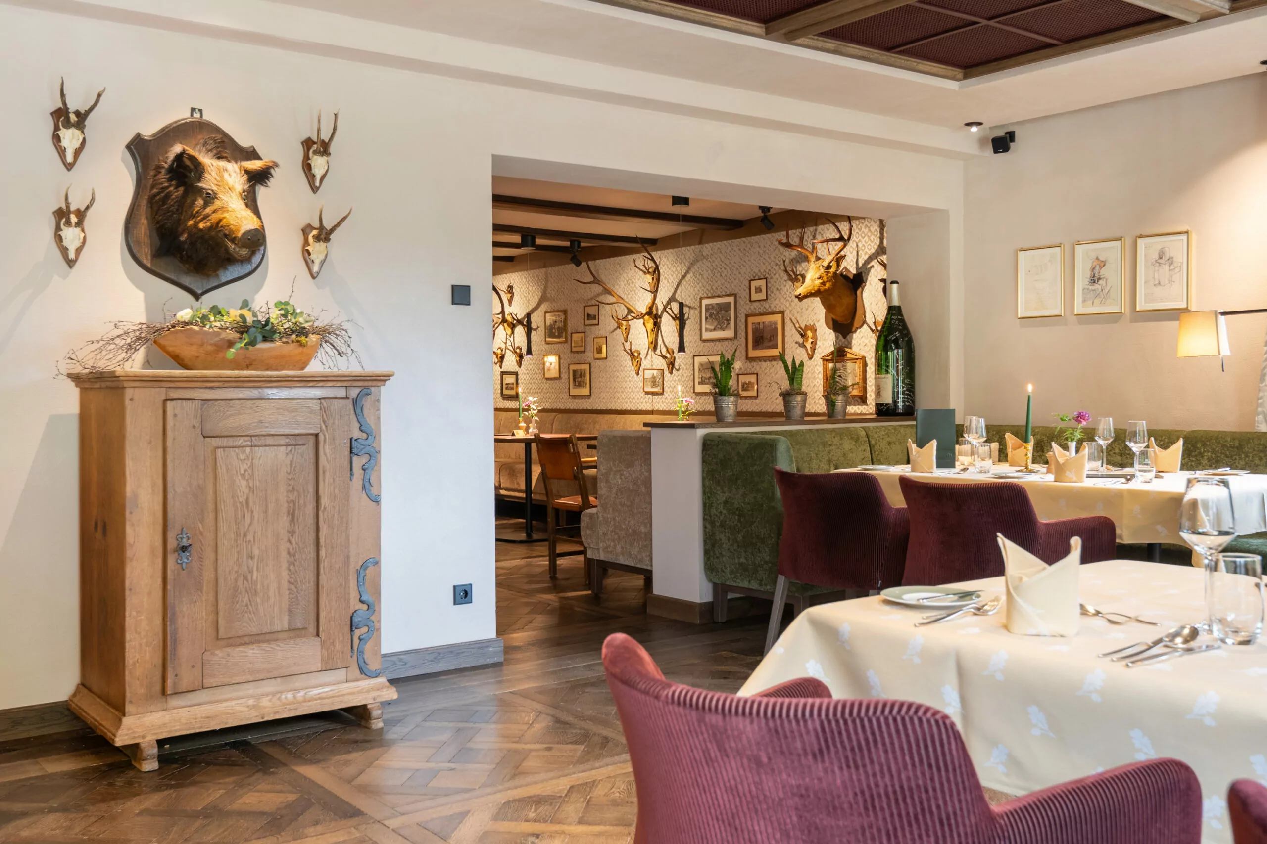 Jagdhaus Wiese Traditionell-modern gestaltetes Restaurant Blick auf gedeckte Tische im Restaurant, im Hintergrund hängen Bilder und Geweihe an der Wand