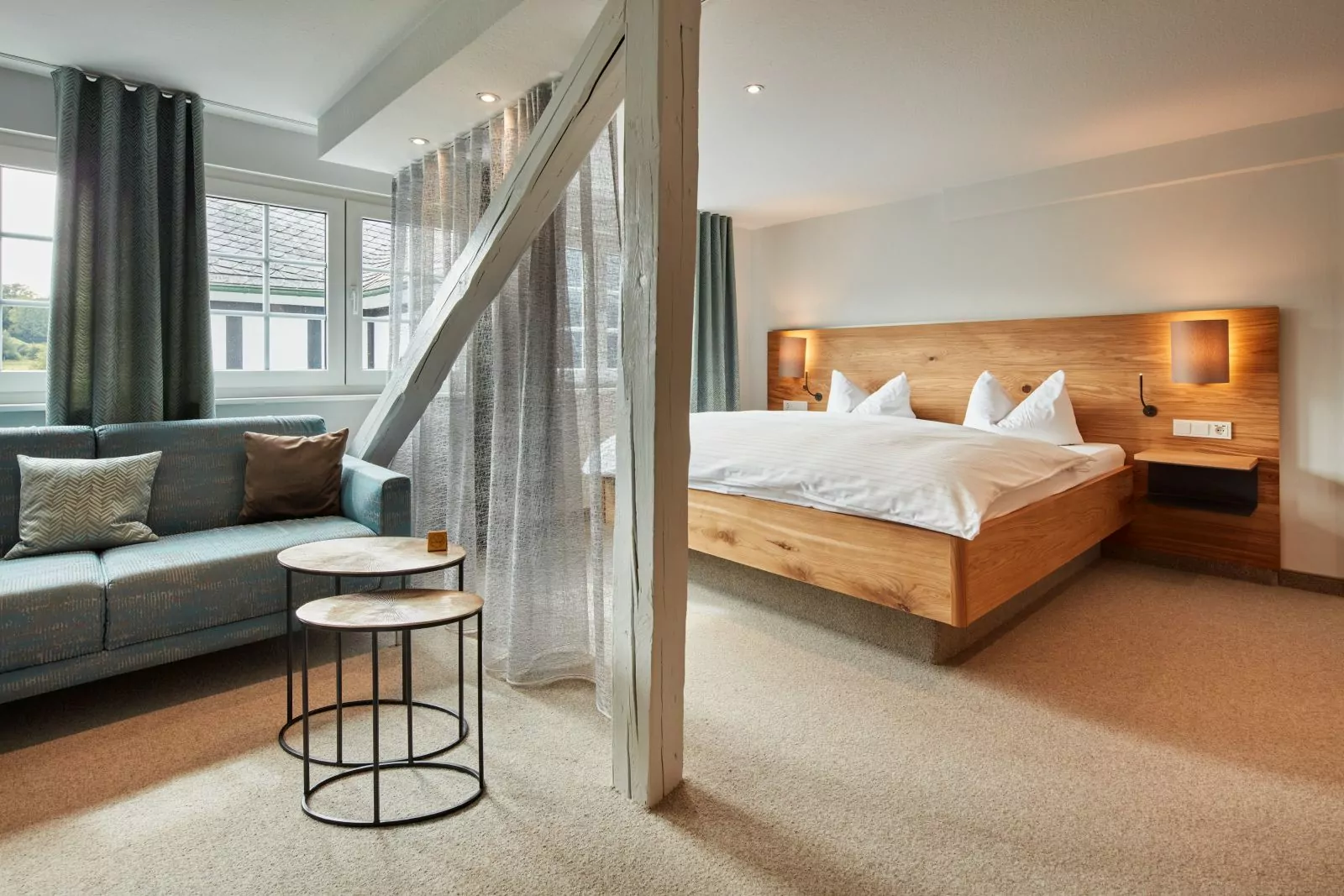 Hotel Platte – Zimmerbeispiel der Kategorie Superior Doppelzimmer mit großem Holzbett und mittig einem Vorhang, der den linken Sitzbereich vom Bett optisch trennt