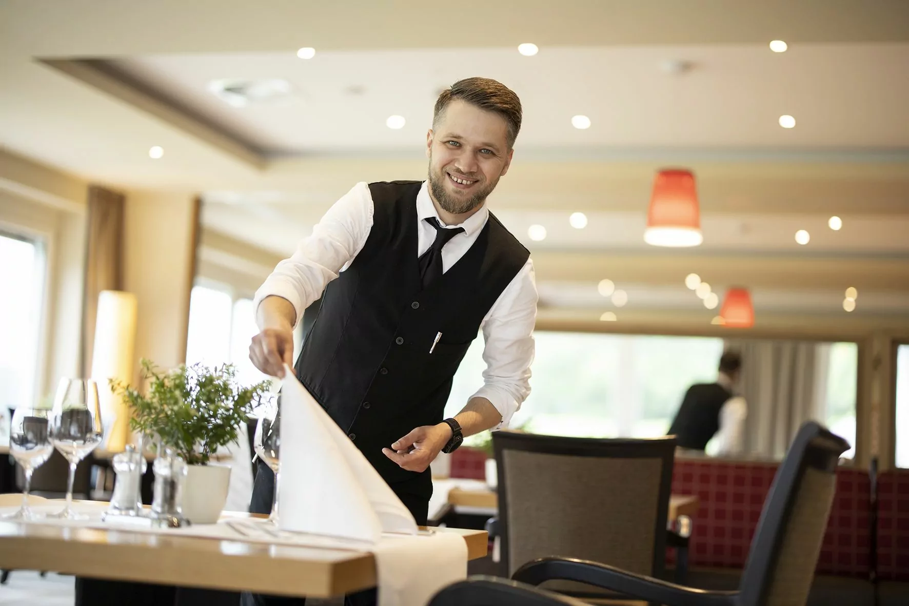 Service-Kollege deckt eine Serviette auf dem Tisch ein