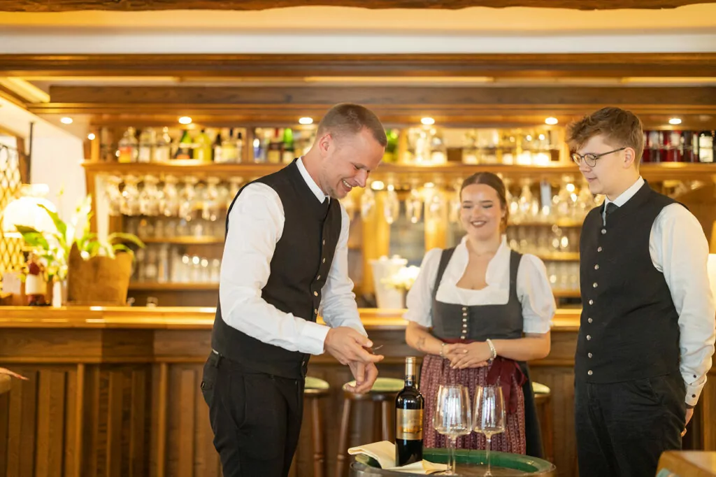 Service im Hotel Voss: ein Mitarbeiter zeigt einem anderen Mitarbeiter und einer Mitarbeiterin, wie man eine Flasche Wein öffnet