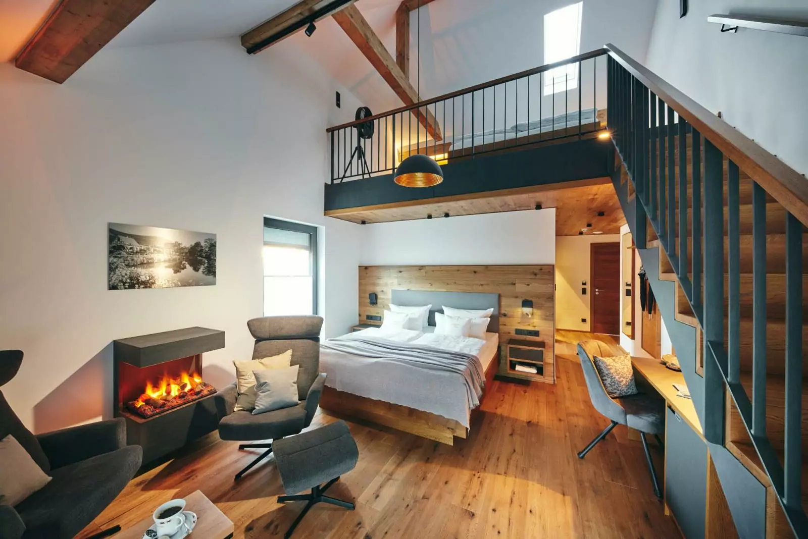Hotel Voss: Suite mit zwei Ebenen, unten Doppelbett, Kaminfeuer, moderne Ohrensessel mit Fußhocker, rechts geht eine Treffe zur oberen Etage mit weiter Schlafgelegenheit