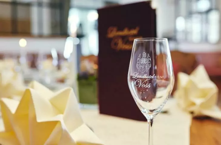 Essen & Trinken im Landhotel Voss leeres Weinglas mit Logo vom Hotel Voss auf gedecktem Tisch