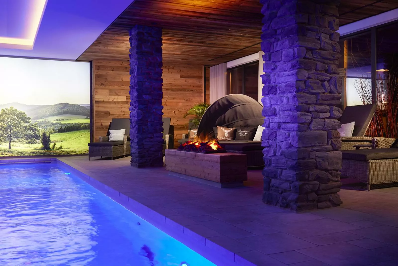 Landhotel Voss – Lichtspiele am Pool Hotel Voss: abendliche Stimmung im Poolbereich, man sieht links den Pool und rechts Ruheliegen