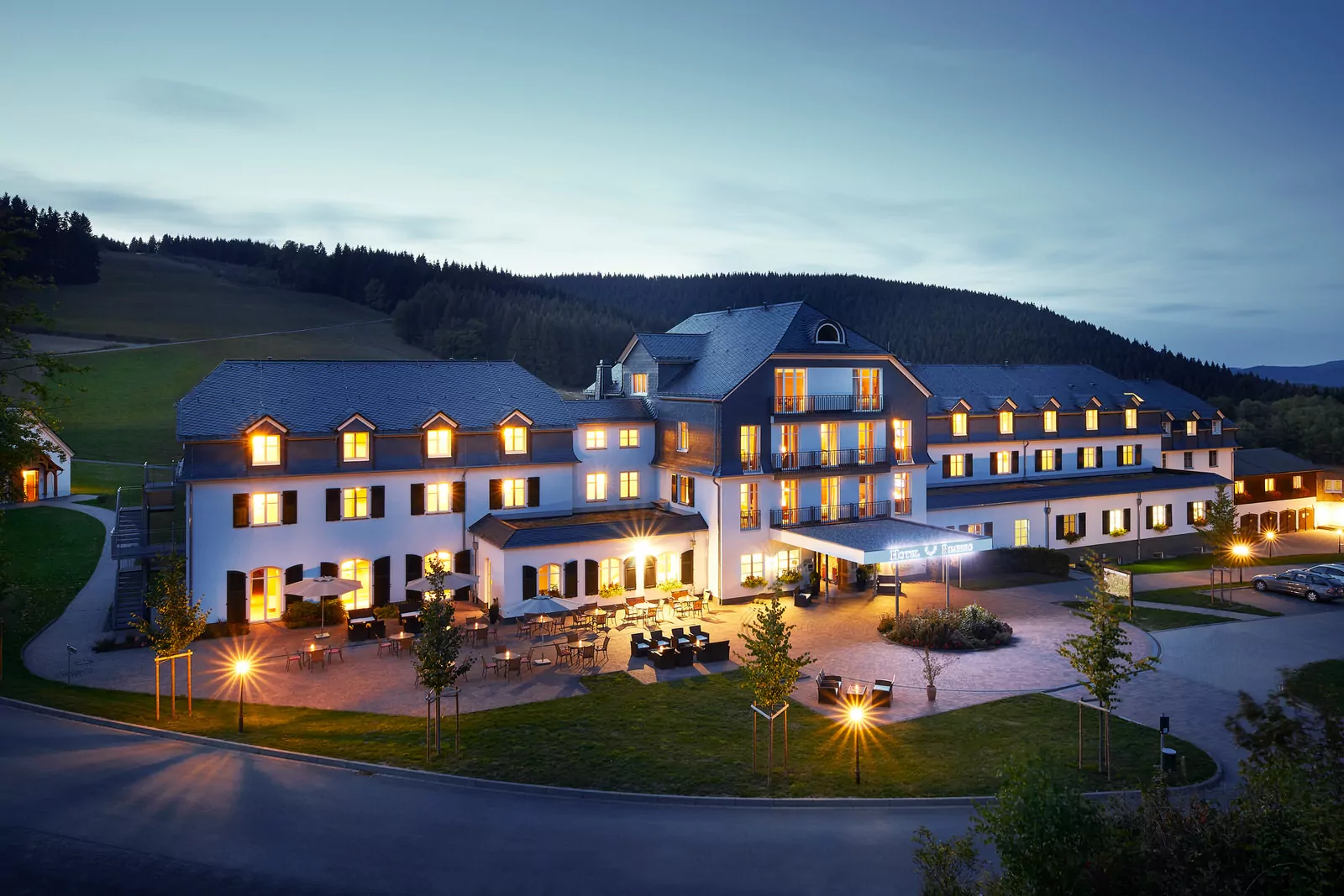 Hotel Rimberg – Abenddämmerung Hotelaußenansicht in der Dämmerung; im Hintergrund sieht man schwach den Rimberg, die Fenster des Hotels sind beleuchtet