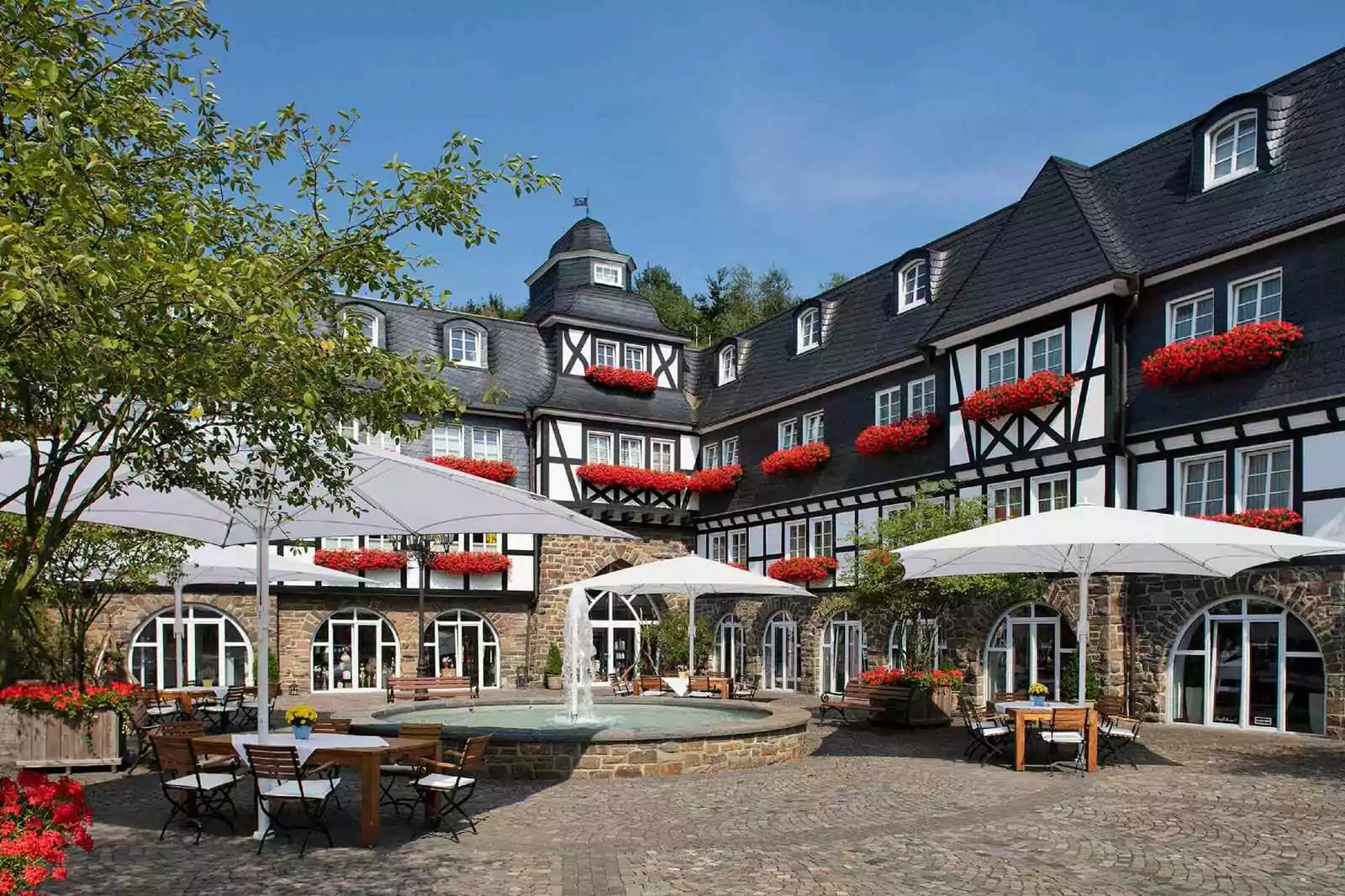 Hotel Deimann – Guthof mit Brunnen Innenhof mit Springbrunnen vom Fachwerk-Gutshof mit Springbrunnen, Tischen und Sonnenschirmen